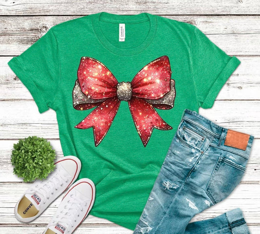 Green t-shirt with a large red bow graphic, paired with jeans and sneakers on a wooden surface.