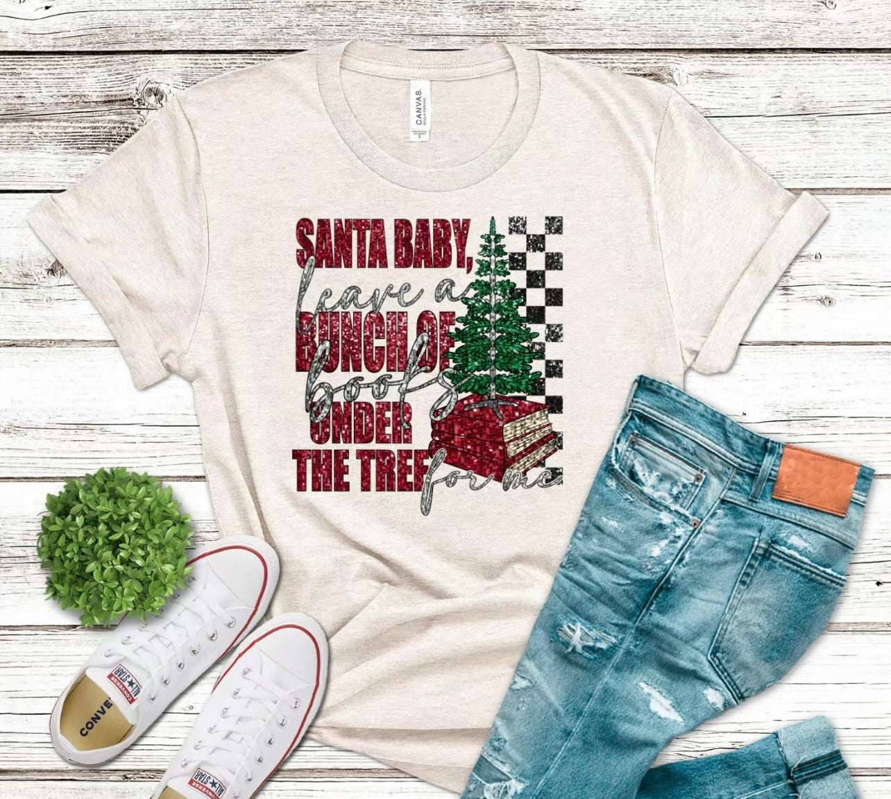 White t-shirt with Christmas-themed graphic, jeans, and white sneakers on a wooden surface